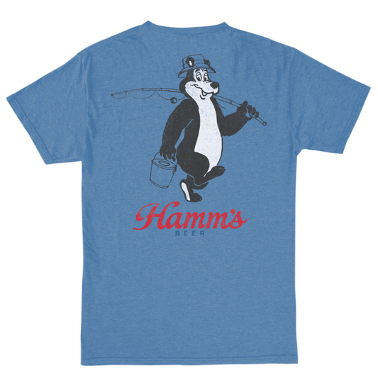 A heather blue short-sleeve t-shirt showing the back graphic, which features a black and white cartoon character holding a fishing rod and bucket, with 'Hamm's BEER' printed in red script below.