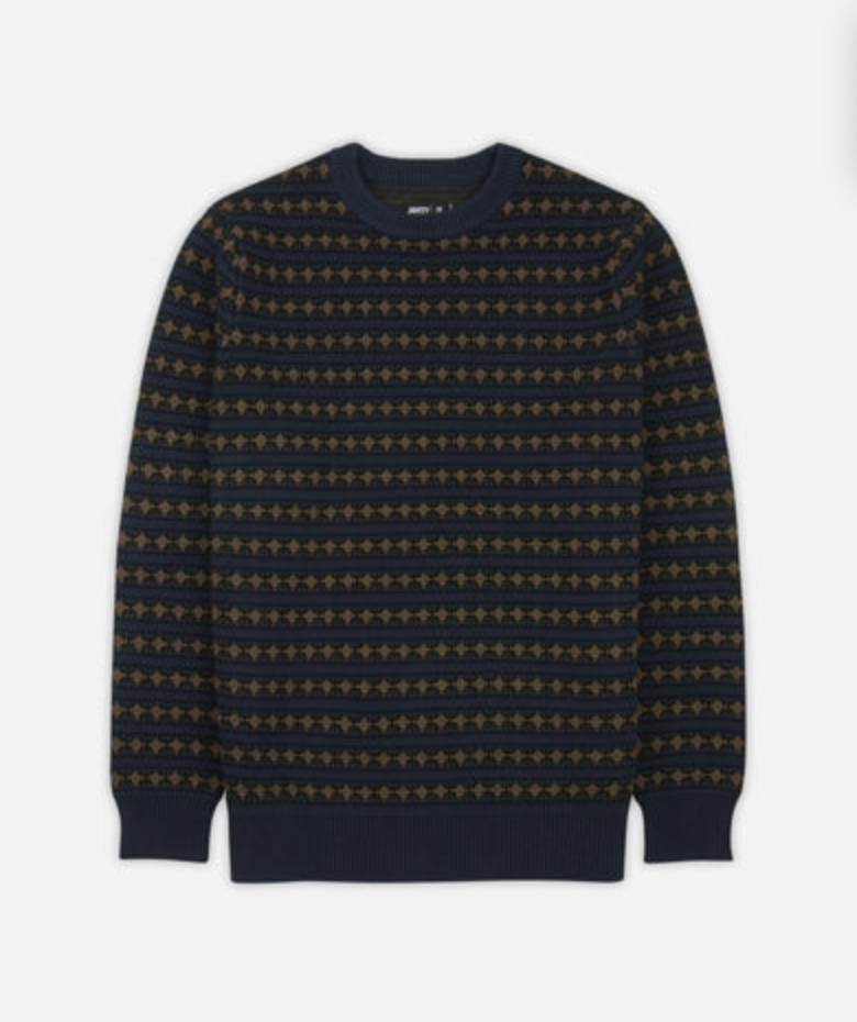 A Jetty Fairisle Stripe navy blue crewneck sweater with horizontal stripes of gold geometric patterns, displayed flat against a light gray background.