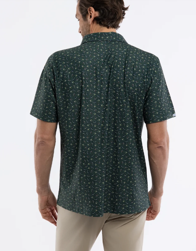 A man viewed from the back wearing a dark green short-sleeve button-up shirt with a small white micro-pattern, paired with beige pants, against a plain white background.