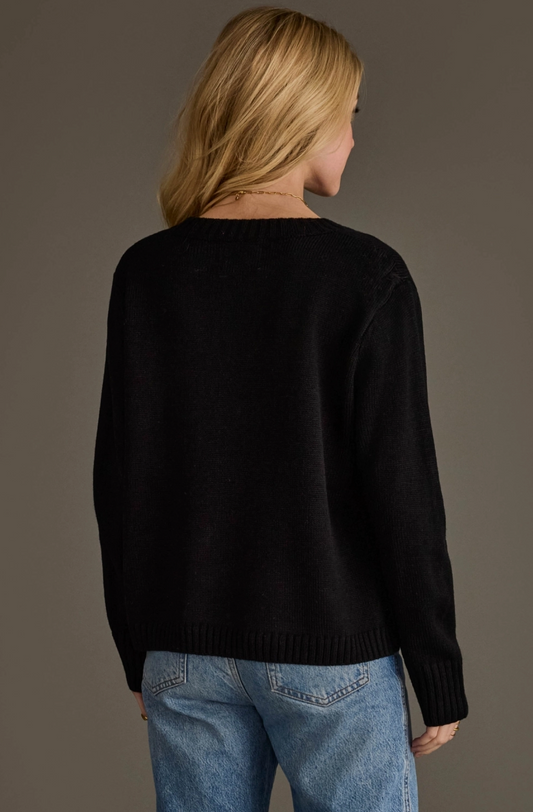 A woman shown from the back wearing a black knit sweater and light blue jeans against a plain taupe studio background.