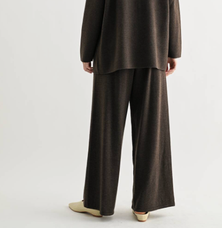 A person shown from the back wearing a matching dark brown knit top and wide-leg pants set, paired with light beige pointed-toe flats, against a plain light gray studio background.