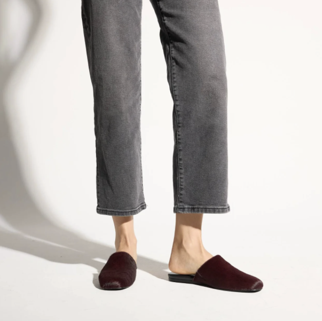 A person wearing dark gray cropped jeans and Yosi Samra Waverly burgundy velvet mule flats, shown from the calves down against a clean white studio background.