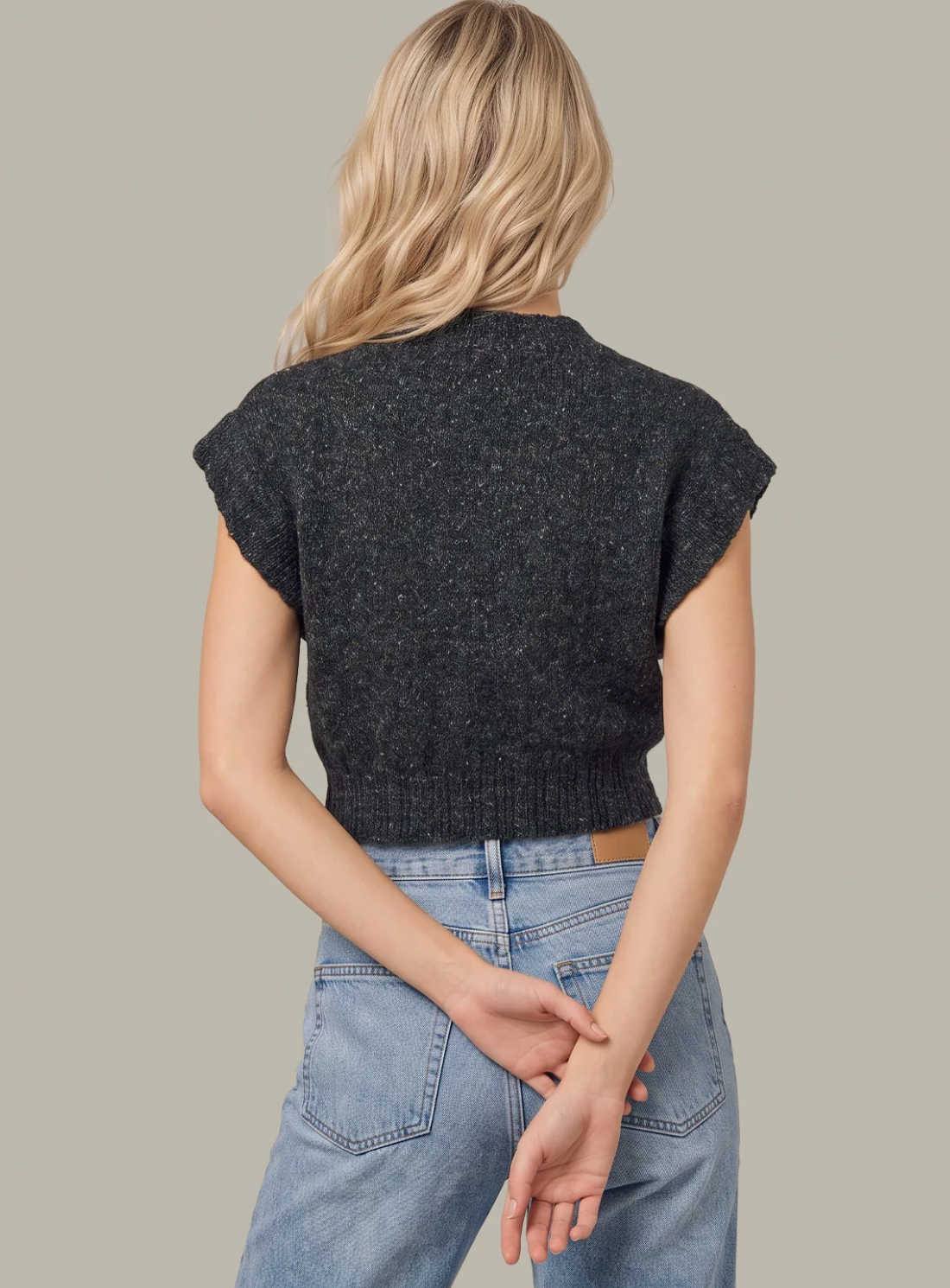 A woman shown from the back wearing a dark charcoal gray short-sleeve 525 America knit sweater and light blue jeans against a solid light gray background.