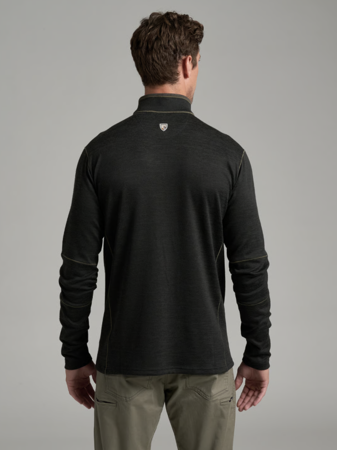 A man viewed from the back wearing a Kuhl Ryzer dark charcoal gray long-sleeve quarter-zip pullover with a small shield logo on the upper neck, paired with khaki pants, against a solid gray studio background.