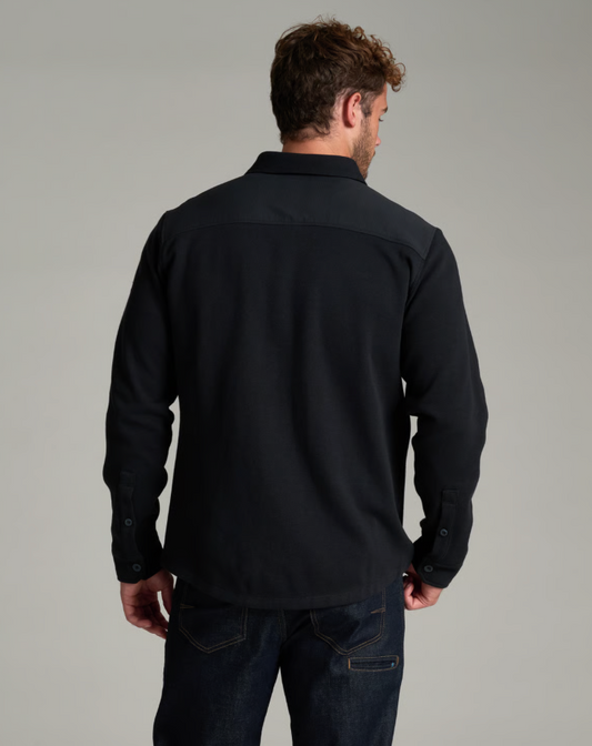 A man viewed from the back wearing a black Kuhl TRelentr standing against a neutral gray studio background.