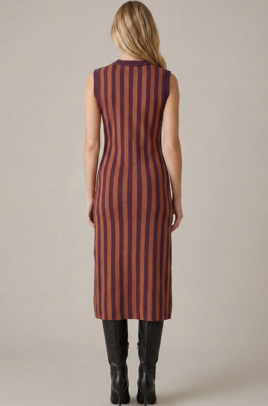 A woman viewed from the back wearing a sleeveless midi dress with vertical rust-brown and dark purple stripes, paired with black knee-high boots, against a neutral light gray background.