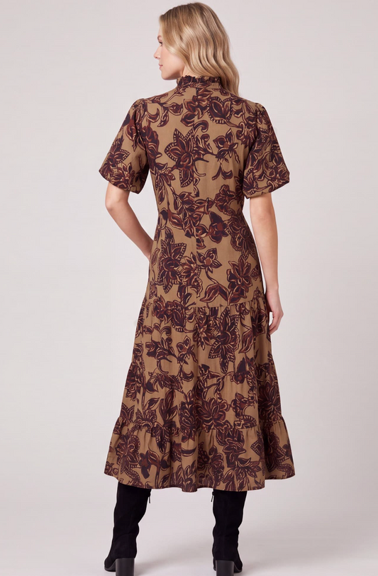 A woman shown from the back wearing a short-sleeve midi dress with a brown and dark red floral pattern on a tan background, paired with black boots, against a light gray studio background.
