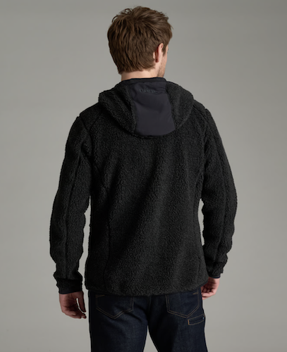 A man viewed from behind wearing a black Kuhl Skapegoat sherpa fleece hooded jacket with a contrasting dark gray hood lining, paired with dark blue jeans, against a solid gray studio background.