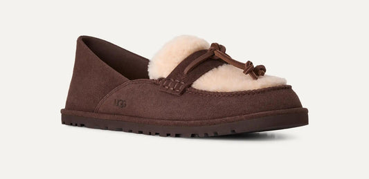 A single UGG Zora slip-on loafer in dark brown suede with a cream-colored shearling lining and a matching brown leather tassel detail, shown against a light off-white background.