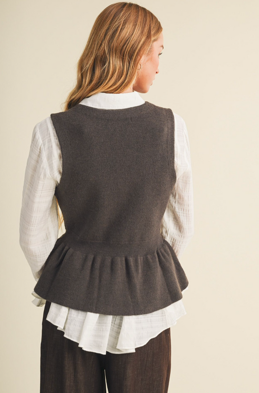 A woman models the back side of a dark brown knit vest layered over a white collared shirt and white ruffled blouse, paired with dark brown trousers, against a solid light beige background.