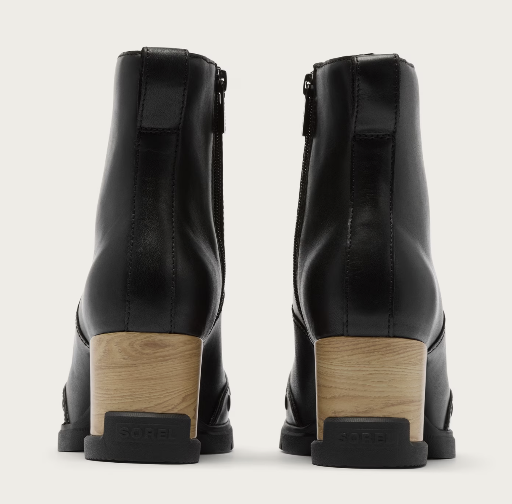 A pair of Sorel waterproof black leather ankle boots shown from the back, featuring a light wood block heel and a black sole with the brand name 'Sorel' embossed on the heel cap, set against a plain off-white background.