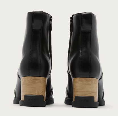 A pair of Sorel waterproof black leather ankle boots shown from the back, featuring a light wood block heel and a black sole with the brand name 'Sorel' embossed on the heel cap, set against a plain off-white background.