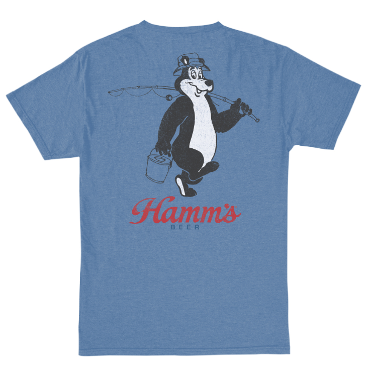 A heather blue short-sleeve t-shirt showing the back graphic, which features a black and white cartoon character holding a fishing rod and bucket, with 'Hamm's BEER' printed in red script below.