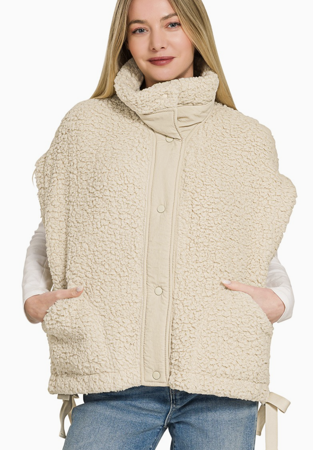 A woman wearing a cream-colored sherpa fleece sleeveless vest with a high mock neck, snap-button front, and side pockets, paired with blue jeans against a plain white background.