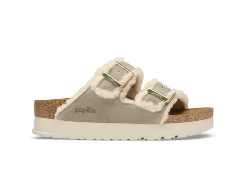 A single Papillo slide sandal in light taupe suede with cream sherpa lining and gold-tone buckle straps, shown from the side on a white background.