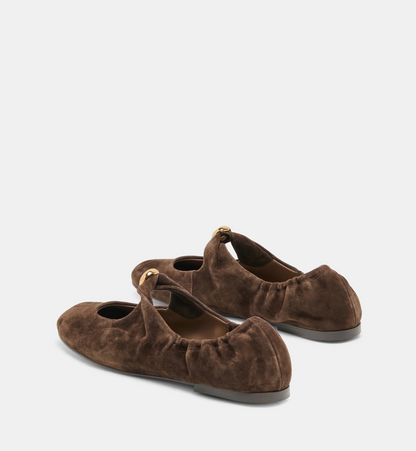 A pair of Dolce Vita Cornel brown suede ballet flats with a small gold-tone metal accent on the strap, shown from a three-quarters angle on a light gray background.