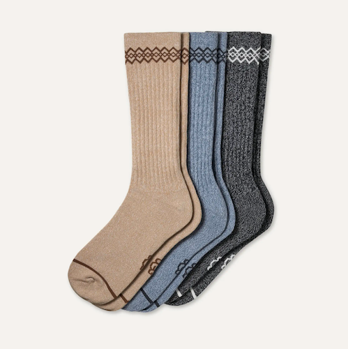 Three pairs of UGG ribbed crew socks in beige, dusty blue, and dark gray, each featuring a geometric patterned cuff and a matching toe cap, displayed against a light off-white background.