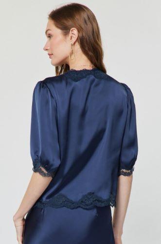 A woman shown from the back wearing a navy blue satin blouse with lace trim at the collar and cuffs, paired with a matching navy skirt, against a light gray studio background.