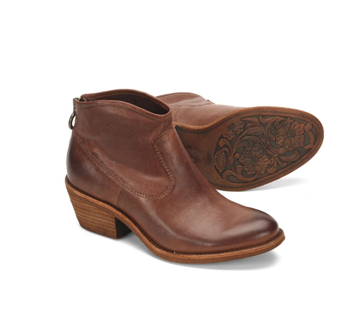 A pair of Sofft Aisley brown leather ankle boots with low stacked heels, shown on a clean white background. One boot is positioned upright to show the side and toe, while the other is turned to display the carved floral pattern on the outsole.