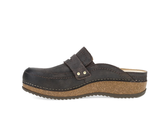 A Dansko dark brown suede clog shoe with a wide strap across the top, secured by two silver metal rivets, and a thick textured cork wedge heel, shown from a side profile on a white background.