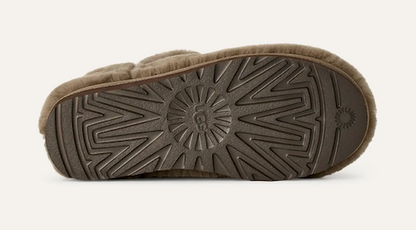 The bottom sole of a UGG Classic Ultra Mini slipper, showing a dark brown textured rubber tread with the brand's signature sunburst pattern and embossed UGG logo, finished with a light brown fuzzy trim.