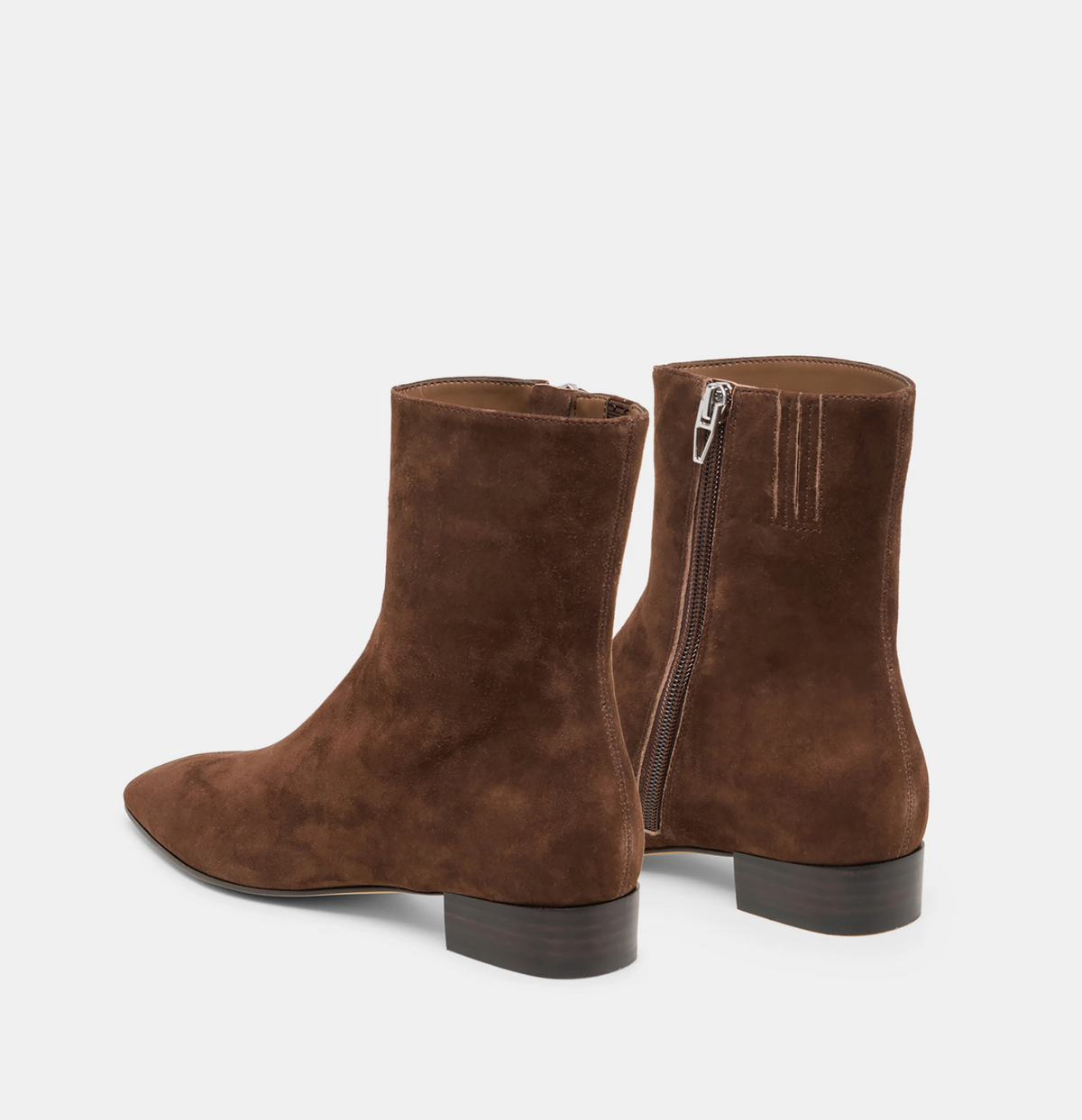 A pair of Dolce Vita Tarine brown suede ankle boots with side zippers, shown from a rear three-quarter angle against a light gray background.