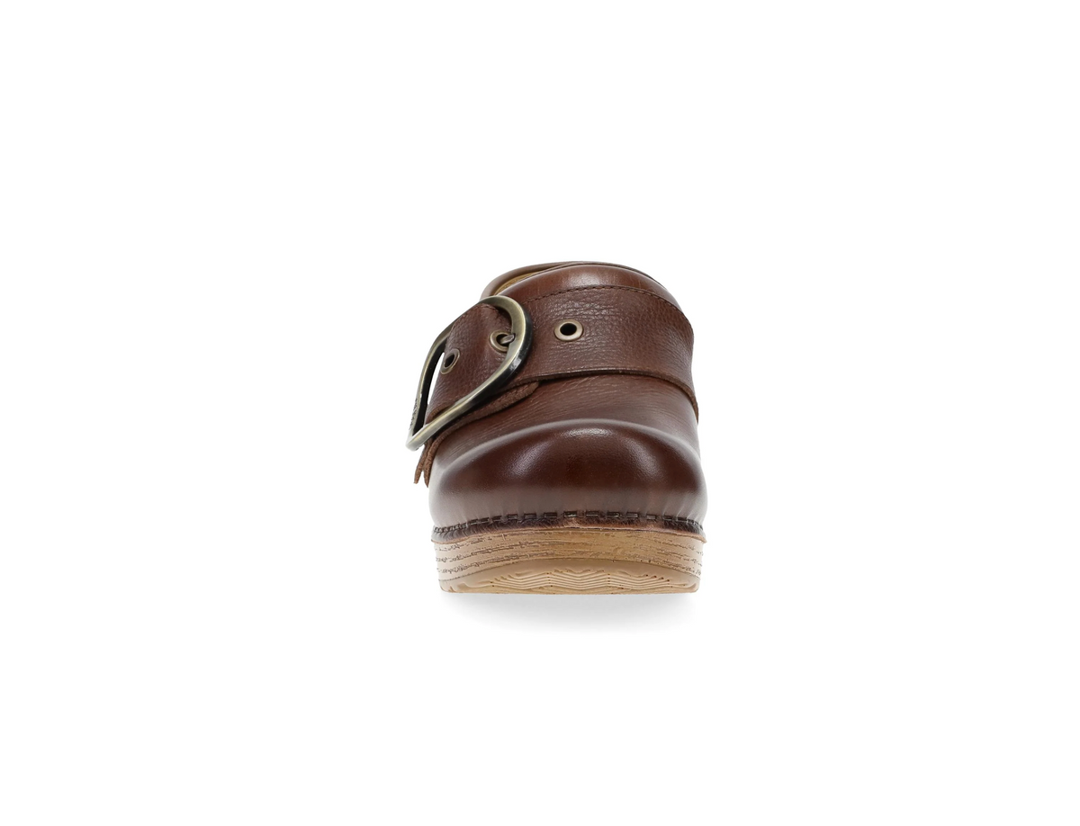 A single brown leatherDansko clog shown from the front, featuring a large metal buckle strap, eyelets, and a light-colored wooden sole on a plain white background.