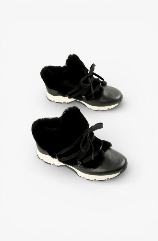 A pair of black low-top lace-up sneakers with plush black faux-fur trim around the collar and a thick white midsole, shown on a light gray background.