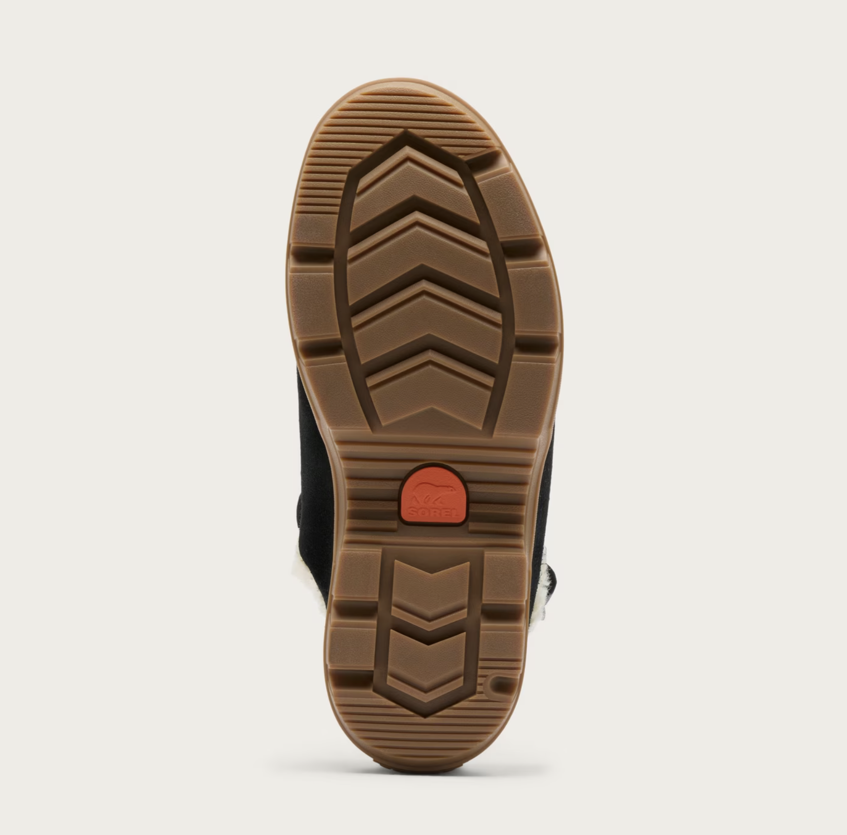The treaded brown rubber outsole of a Sorel clog, showing a small orange-red circular logo in the center, photographed against a light gray background.