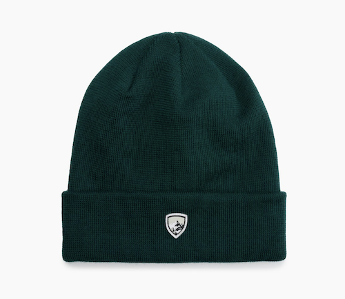 A dark green Kuhl merino ribbed beanie hat with a folded cuff, featuring a small white embroidered shield logo on the front, set against a plain white background.
