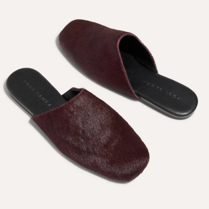 A pair of Yosi Samra Waverly dark burgundy mule slippers with a textured hair-on-hide upper and black soles, displayed on a light cream background.