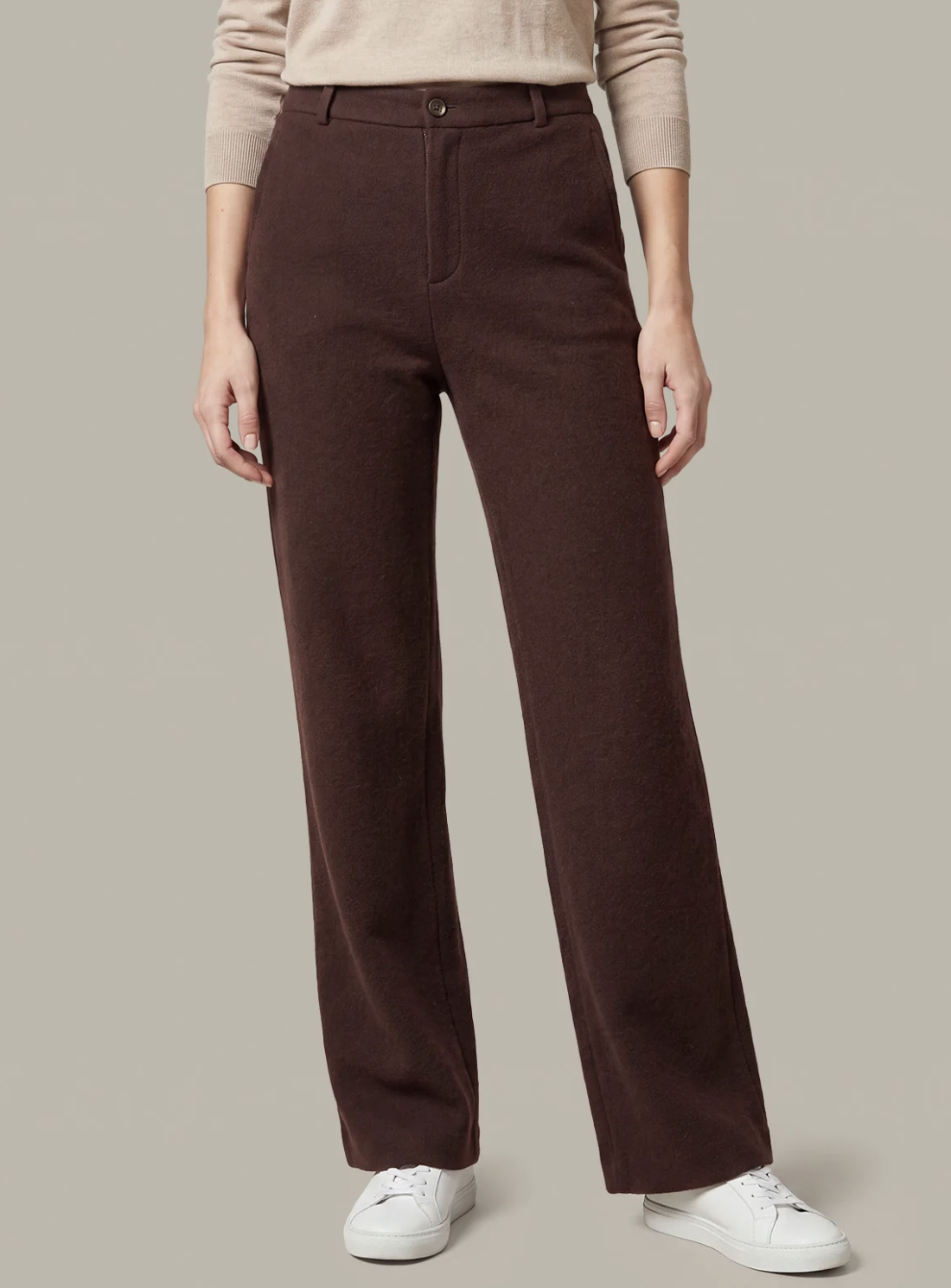 A model wearing dark brown 525 America straight-leg trousers, a beige long-sleeve top, and white sneakers, shown from the waist down against a solid light gray background.