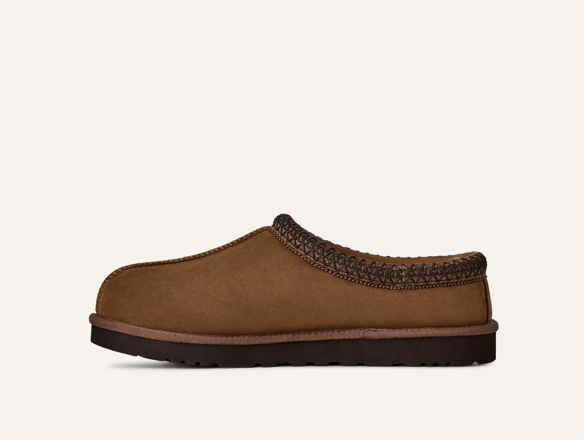 A single UGG Men’s Tasman II Nubuck brown suede slip-on clog shoe with a dark braided trim and a dark sole, shown in profile against a light off-white background.