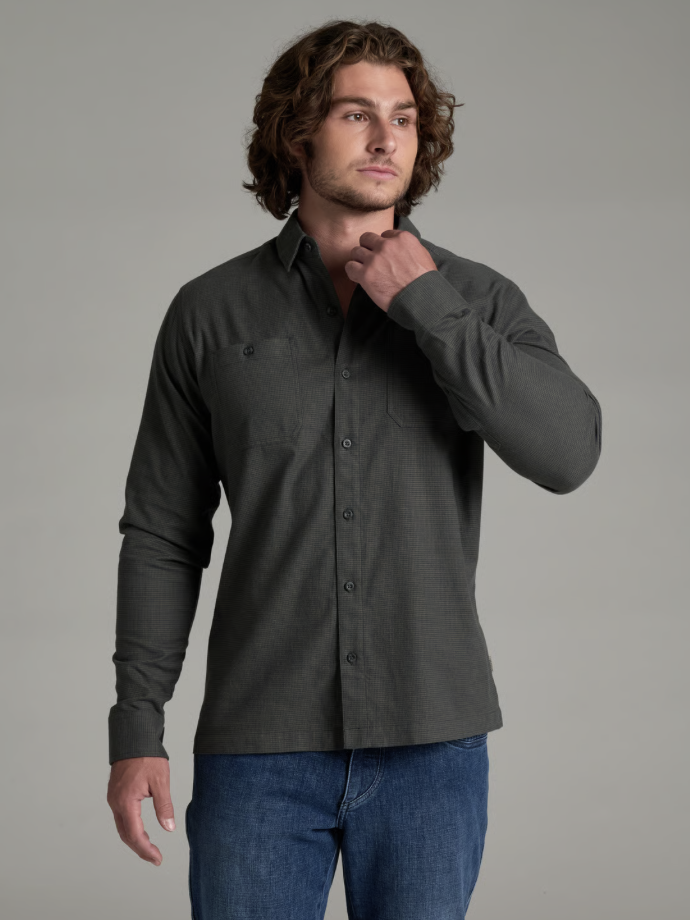 A man wearing a Kuhl Revolvr  dark charcoal gray long-sleeve button-down shirt and blue jeans, posing against a solid gray studio background.