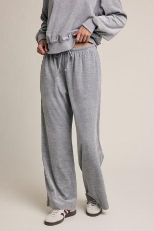 A person wearing loose gray sweatpants with a drawstring waist, paired with a matching gray sweatshirt and white sneakers, photographed against a plain light beige studio background.