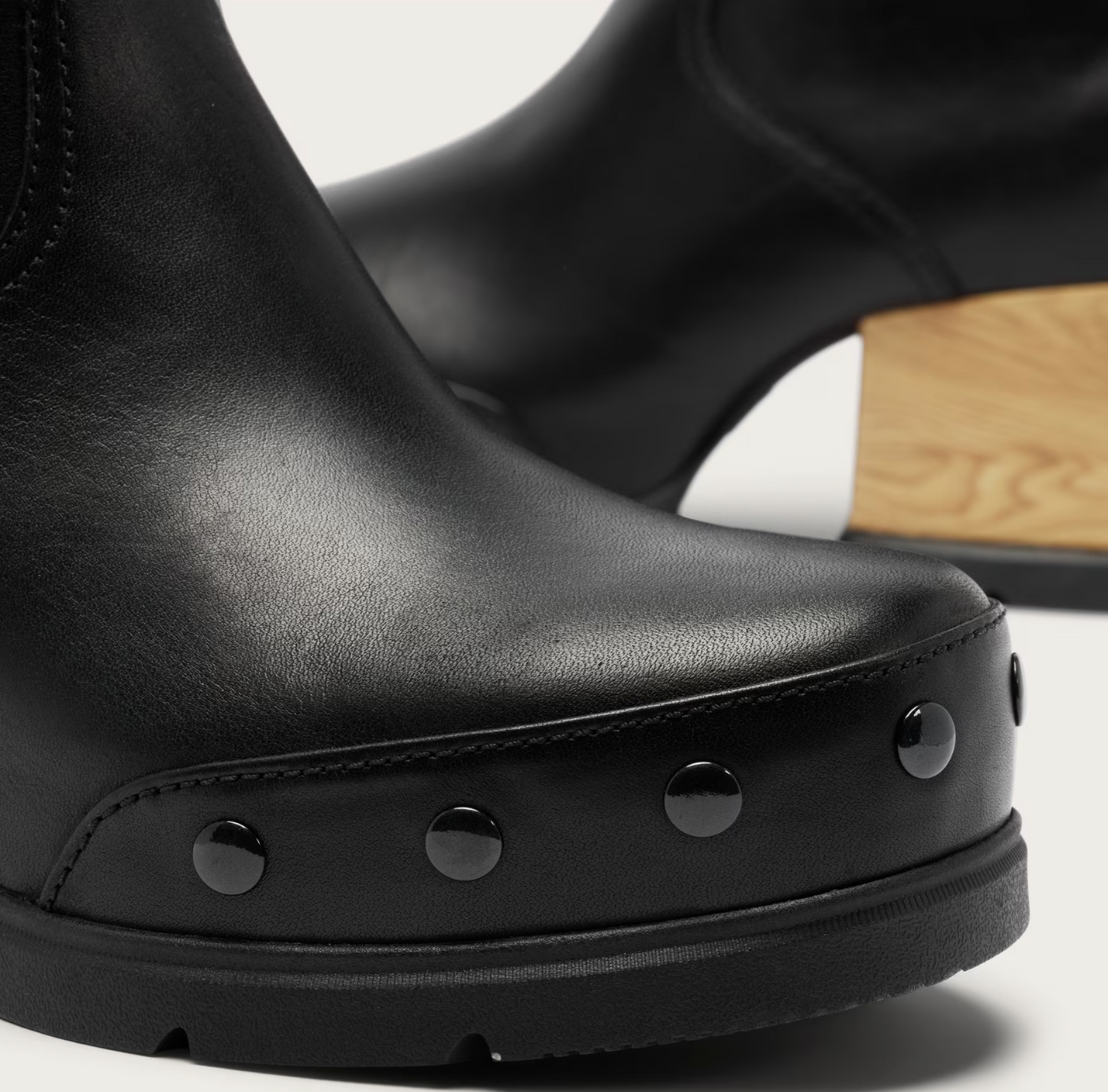 Close-up of a Sorel waterproof black leather ankle boot with a chunky platform sole, black rivet studs, and a light wood block heel on a white background.