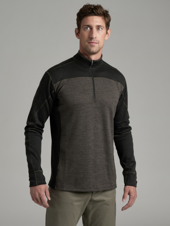 A man wearing a Kuhl Ryzer dark gray and black quarter-zip long-sleeve athletic shirt, paired with olive green pants, photographed against a solid gray studio background.