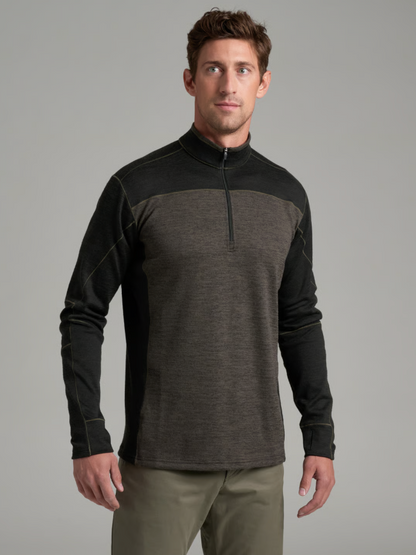 A man wearing a Kuhl Ryzer dark gray and black quarter-zip long-sleeve athletic shirt, paired with olive green pants, photographed against a solid gray studio background.