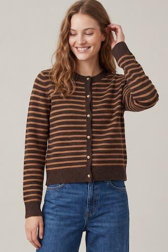 A woman wearing a brown and tan striped button-up cardigan sweater with blue jeans, posing against a neutral light gray background.