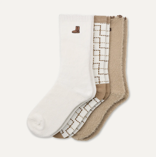 Three pairs of UGG crew socks fanned out on a light cream background: one white pair with a small brown boot logo, one cream pair with a brown dotted grid pattern, and one beige fuzzy pair.