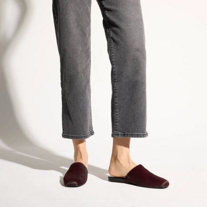 A person wearing dark gray cropped jeans and Yosi Samra Waverly burgundy velvet mule flats, shown from the calves down against a clean white studio background.