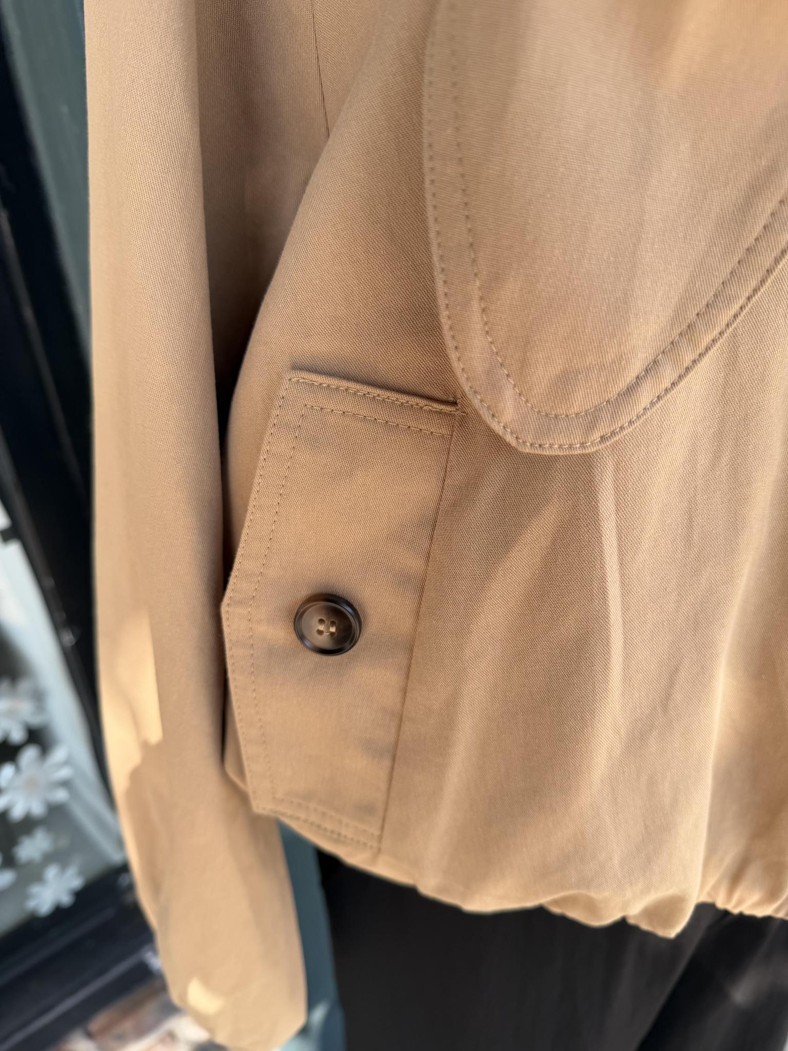 Close-up of a beige or khaki Entro jacket or shirt fabric showing a buttoned chest pocket and part of a curved neckline, photographed against a dark background.