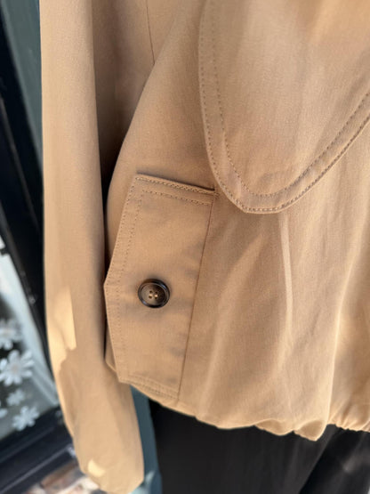 Close-up of a beige or khaki Entro jacket or shirt fabric showing a buttoned chest pocket and part of a curved neckline, photographed against a dark background.