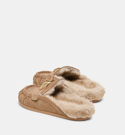 A pair of Dolce Vita Jodero tan suede slip-on flats with fluffy cream faux-fur lining and a small gold-tone decorative accent on the upper, shown against a plain light gray background.