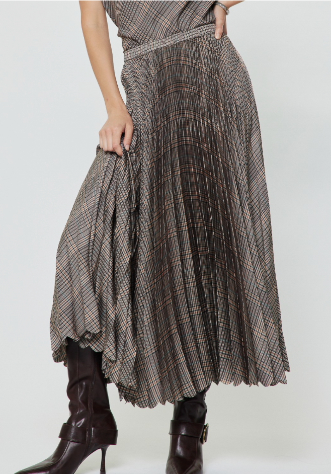 A Current Air pleated high-waisted maxi skirt in a brown and beige plaid pattern, styled with dark brown leather heeled ankle boots against a plain light gray studio background.