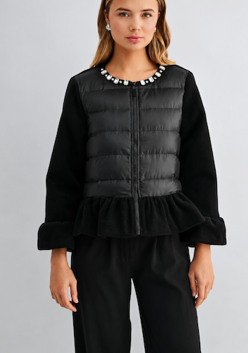 A woman modeling a black quilted puffer vest with a beaded neckline over a black long-sleeve top and black trousers, shot against a light gray studio background.