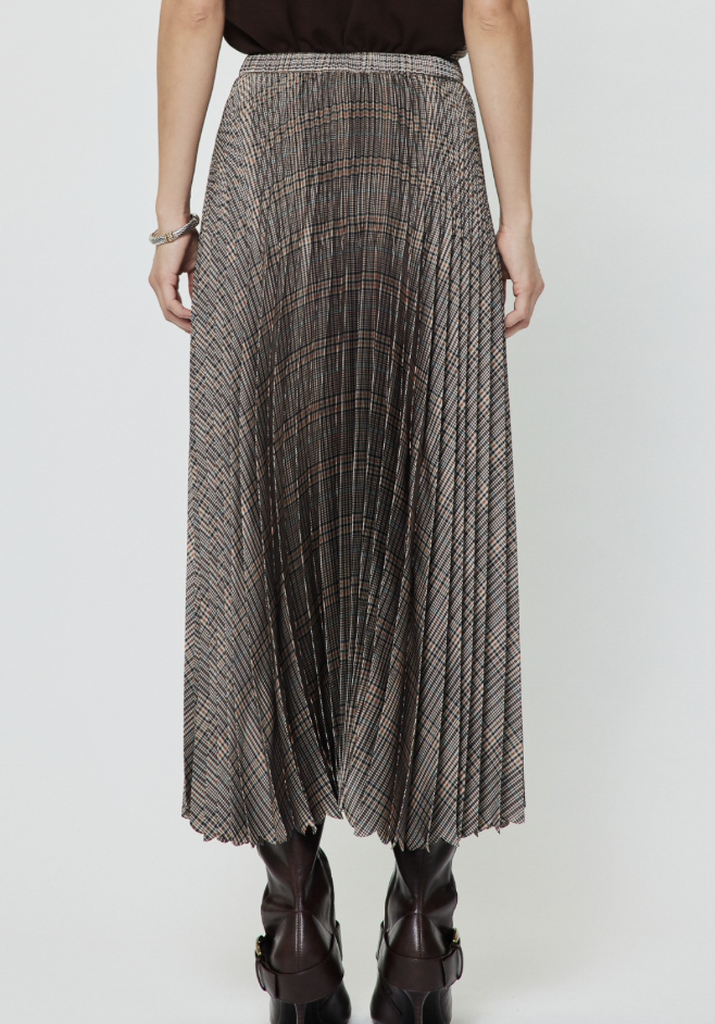 A Current Air pleated midi skirt with a brown, beige, and black plaid pattern, worn by a model with dark brown ankle boots against a light gray studio background.