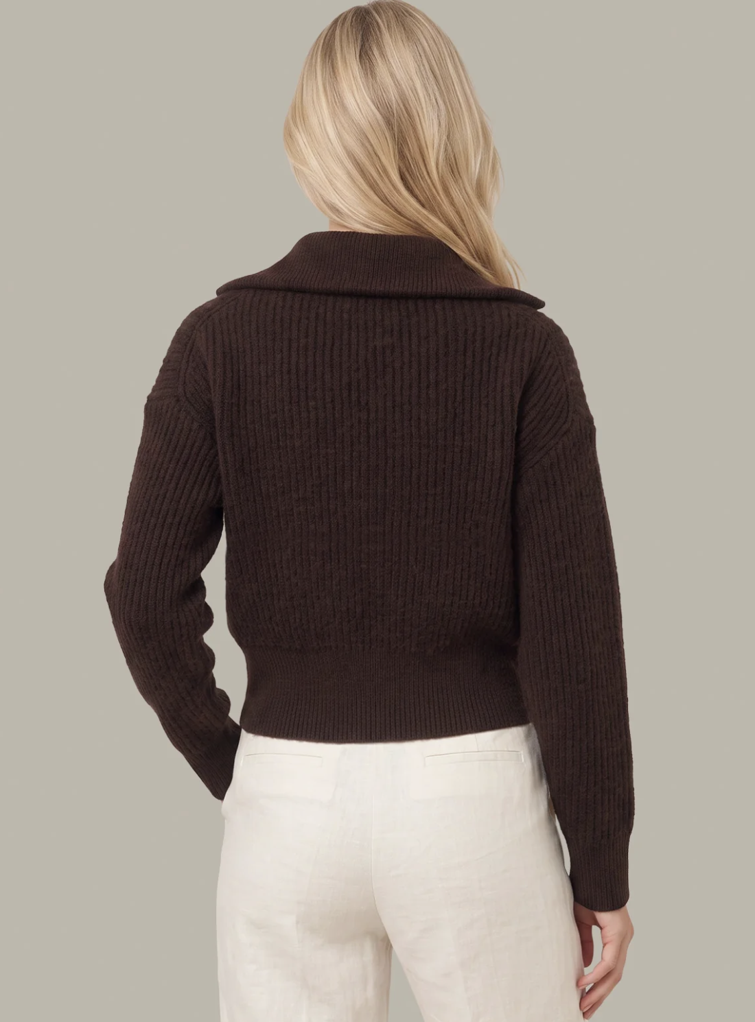 A woman shown from the back wearing a dark brown ribbed knit 525 America sweater with a wide collar and cream-colored pants, set against a solid light gray background.