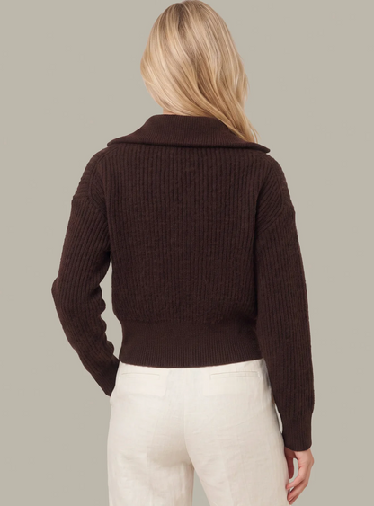 A woman shown from the back wearing a dark brown ribbed knit 525 America sweater with a wide collar and cream-colored pants, set against a solid light gray background.