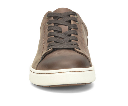 A single low-top leather sneaker shown from the front on a white background. The shoe features a medium brown leather upper, dark brown laces, and a thick white rubber sole.